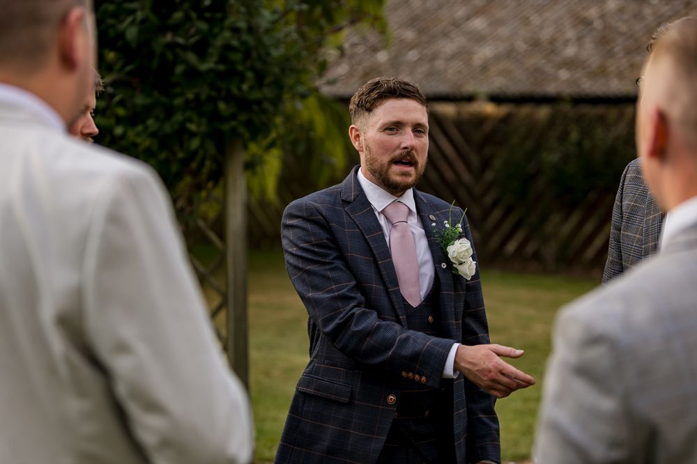 A man in a suit gestures while speaking to others at an outdoor gathering.