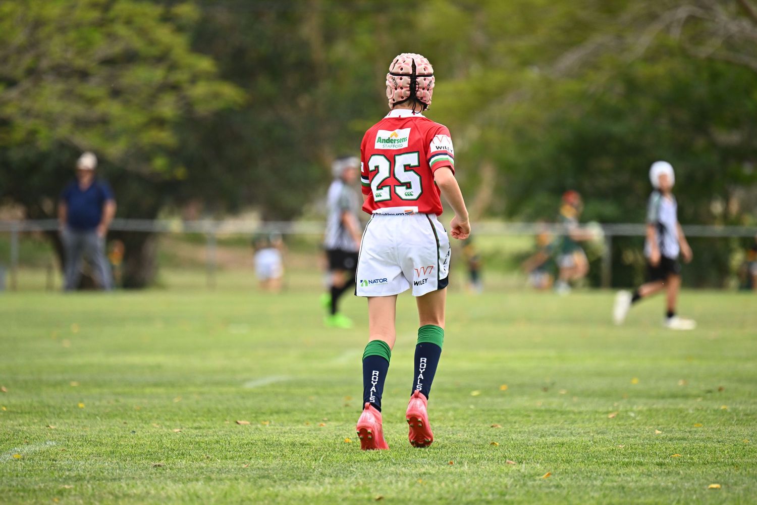 Rugby player in red jersey number 25 stands on grass field during outdoor match.