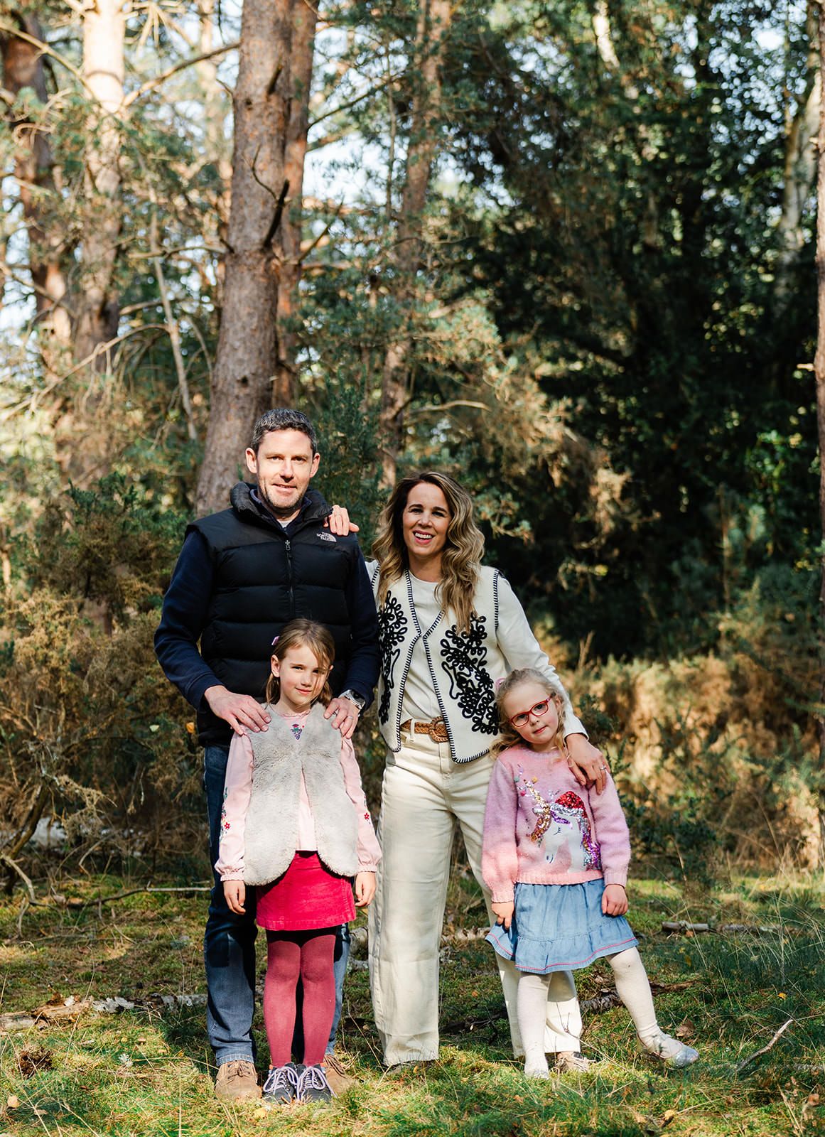 Family enjoying a sunny autumn day together in a wooded area with fallen leaves and pine trees.