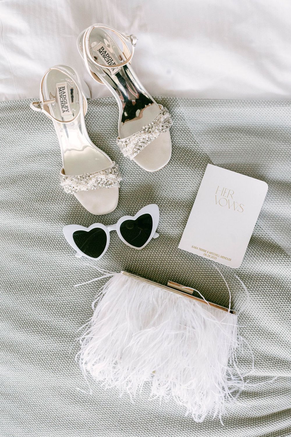 Elegant white feathered bridal accessories including heels, sunglasses and invitation card arranged on light fabric at Landsdowne Resort.