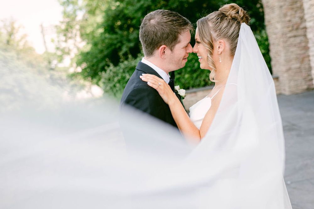 A romantic wedding moment captured in soft focus with a flowing white veil in the foreground.