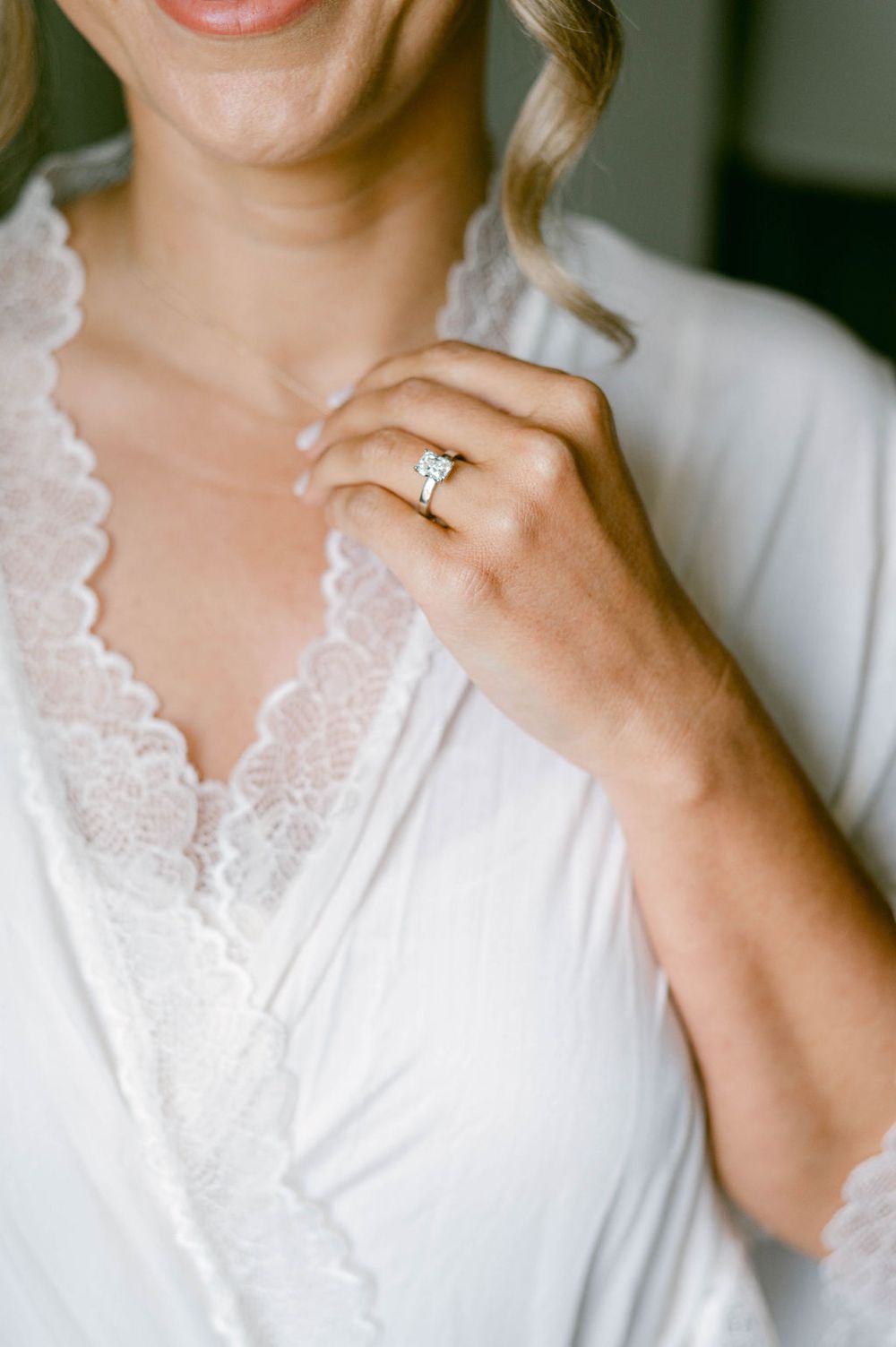 Close-up view of delicate white lace trim on a bridal robe with an elegant engagement ring visible.
