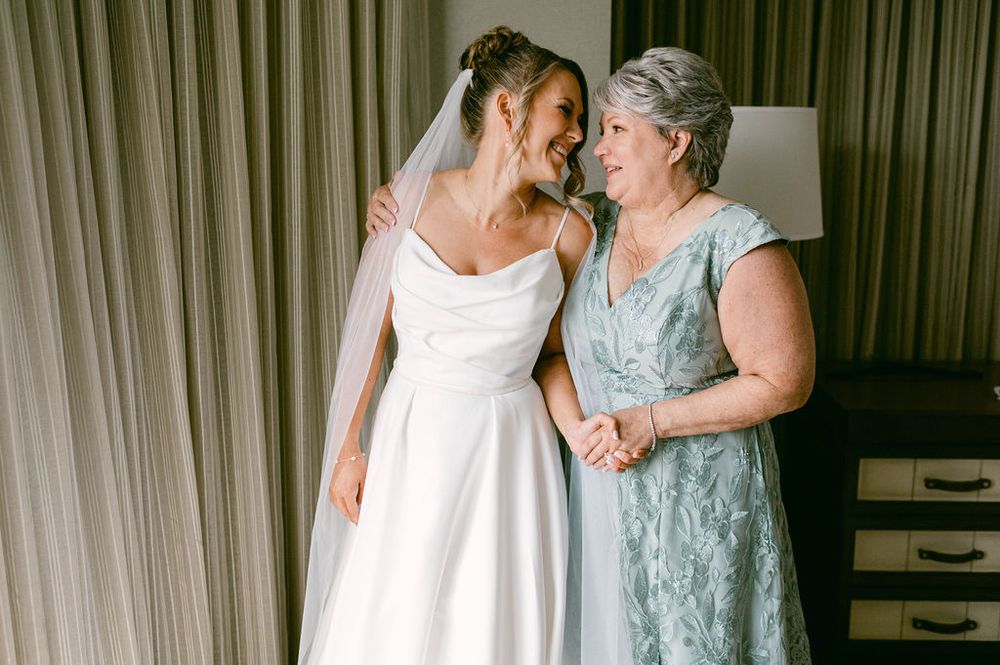 A bride in a white wedding dress and someone in a light blue dress embrace in a tender moment at a wedding.
