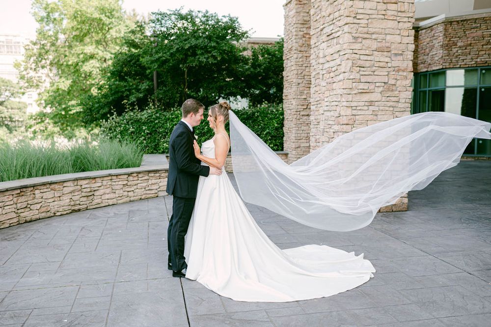 A flowing white wedding veil trails behind a couple on a stone patio during their romantic photo session.