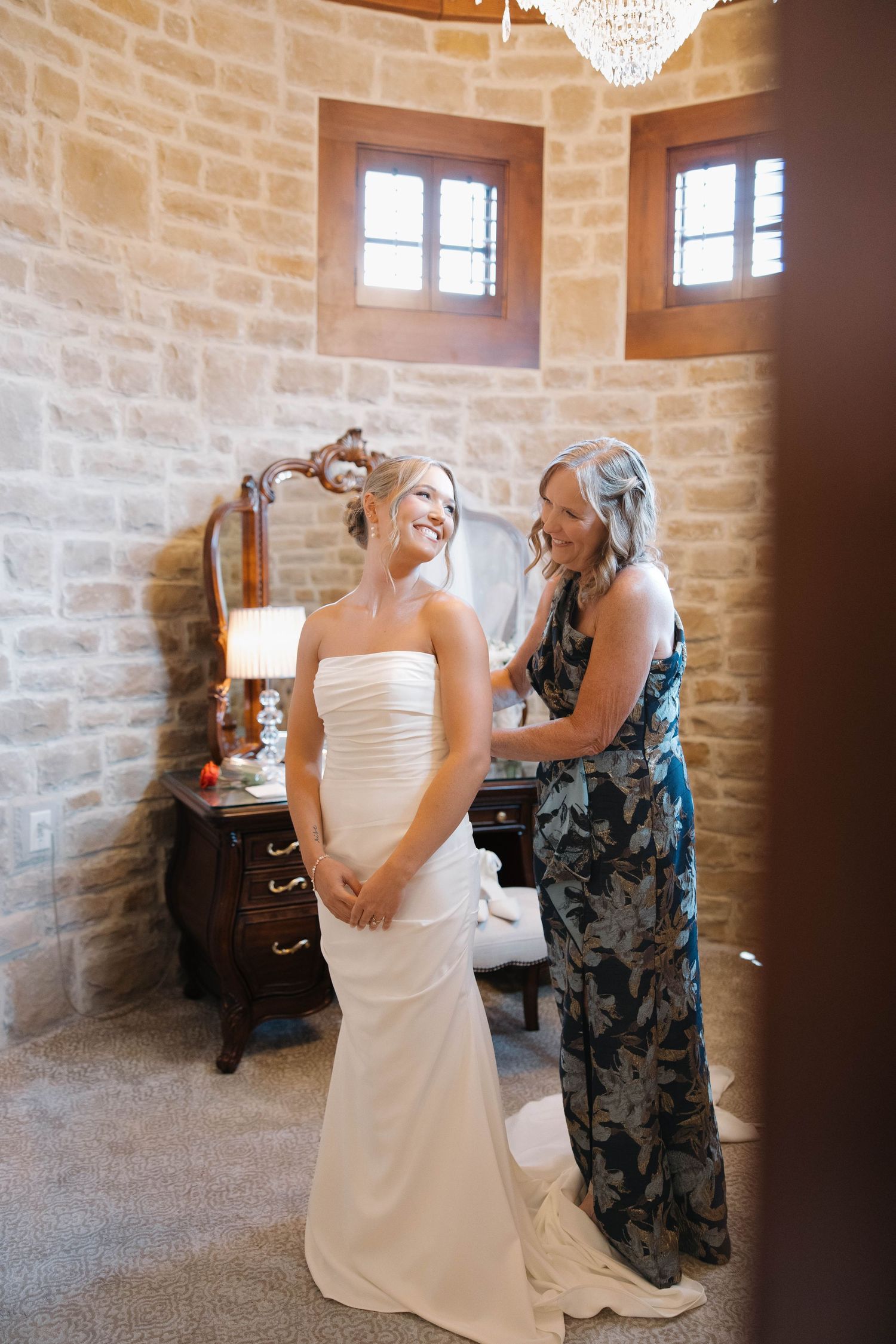 A wedding dress fitting moment in a stone-walled room with elegant decor and natural lighting.