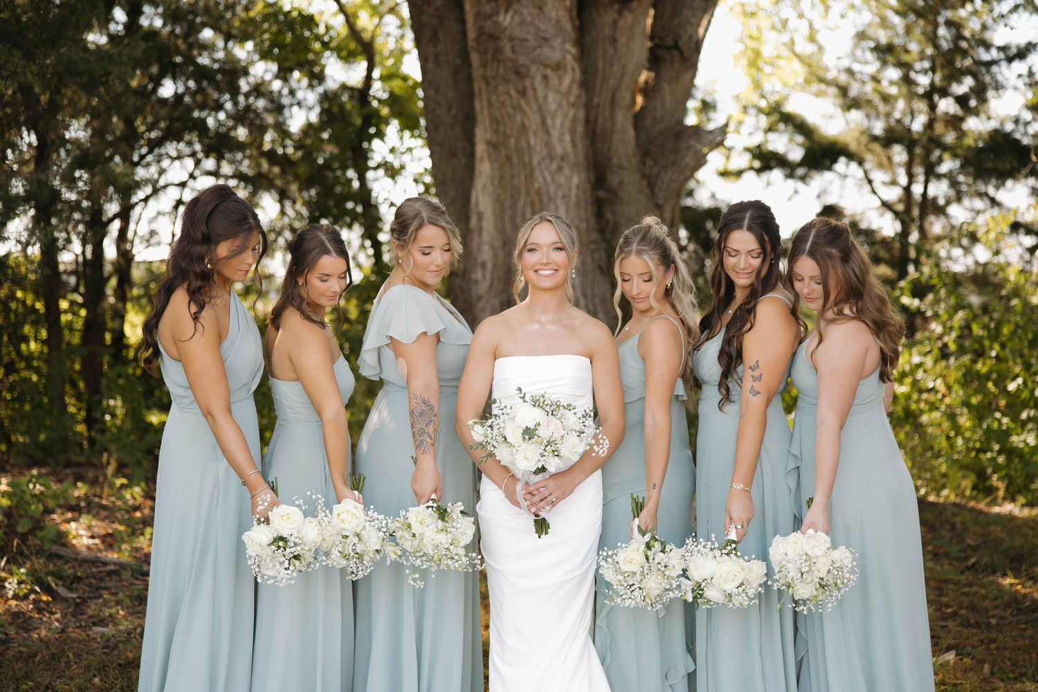 Wedding party poses outdoors with bridesmaids in light blue dresses holding white bouquets.
