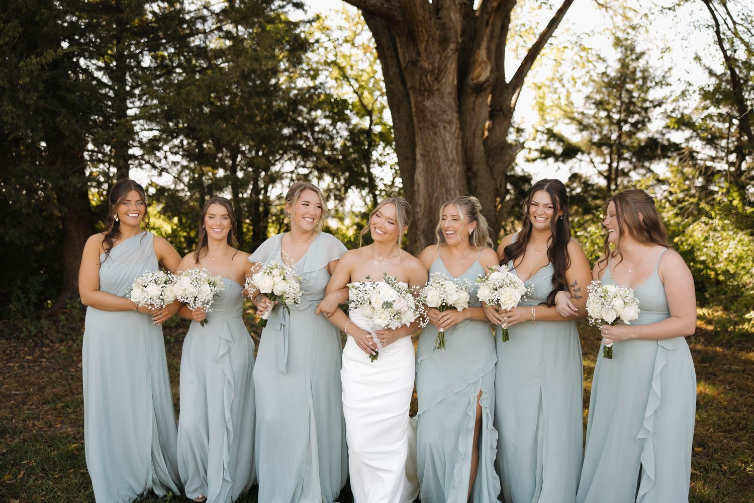 Bridesmaids in pale blue dresses pose with the bride for a sunny outdoor portrait.