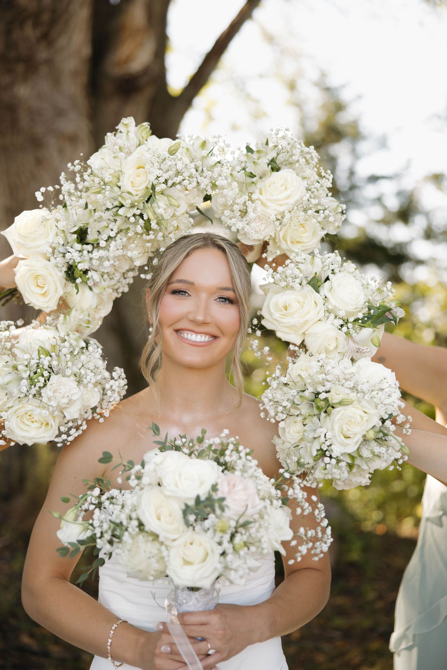 Beautiful white floral bouquet with roses and baby's breath against a sunny outdoor backdrop.
