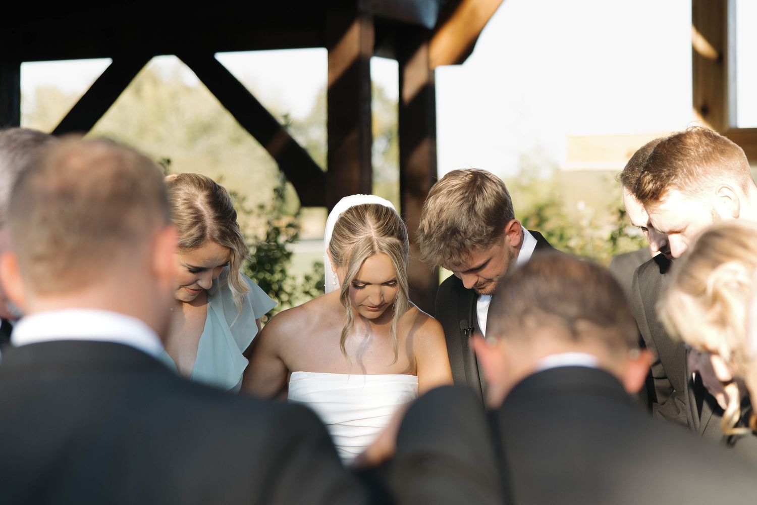 Intimate moment during outdoor wedding ceremony as couple exchanges vows under wooden pavilion.