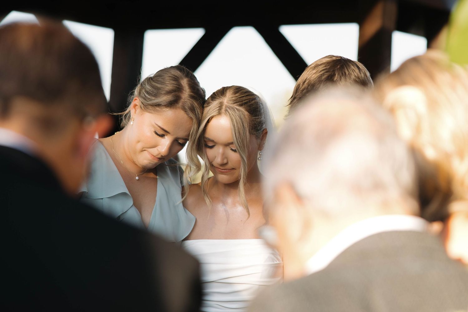 Wedding party members gather closely together during an outdoor ceremony.