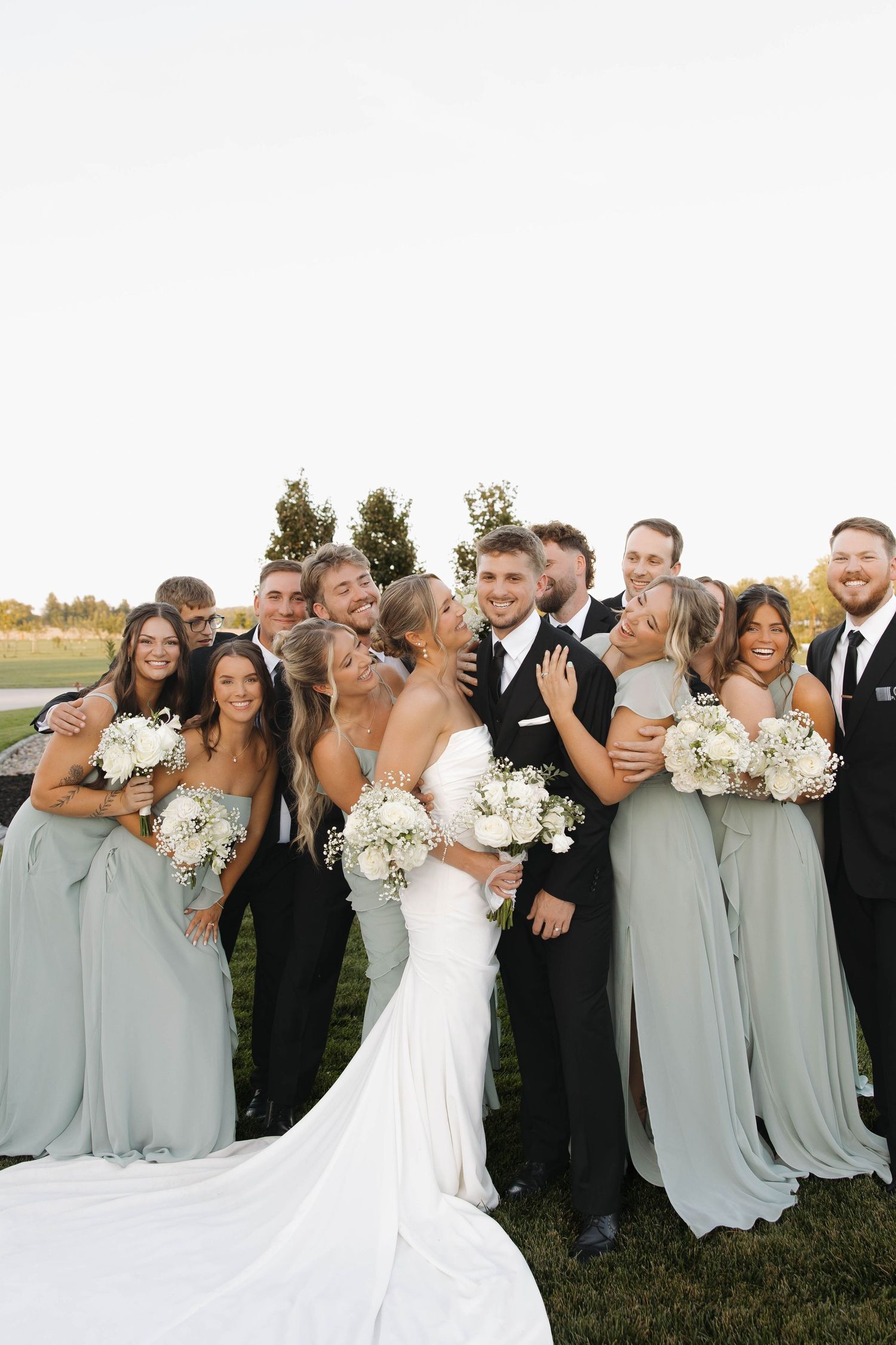 Joyful wedding party laughs together while posing for group photos outdoors.