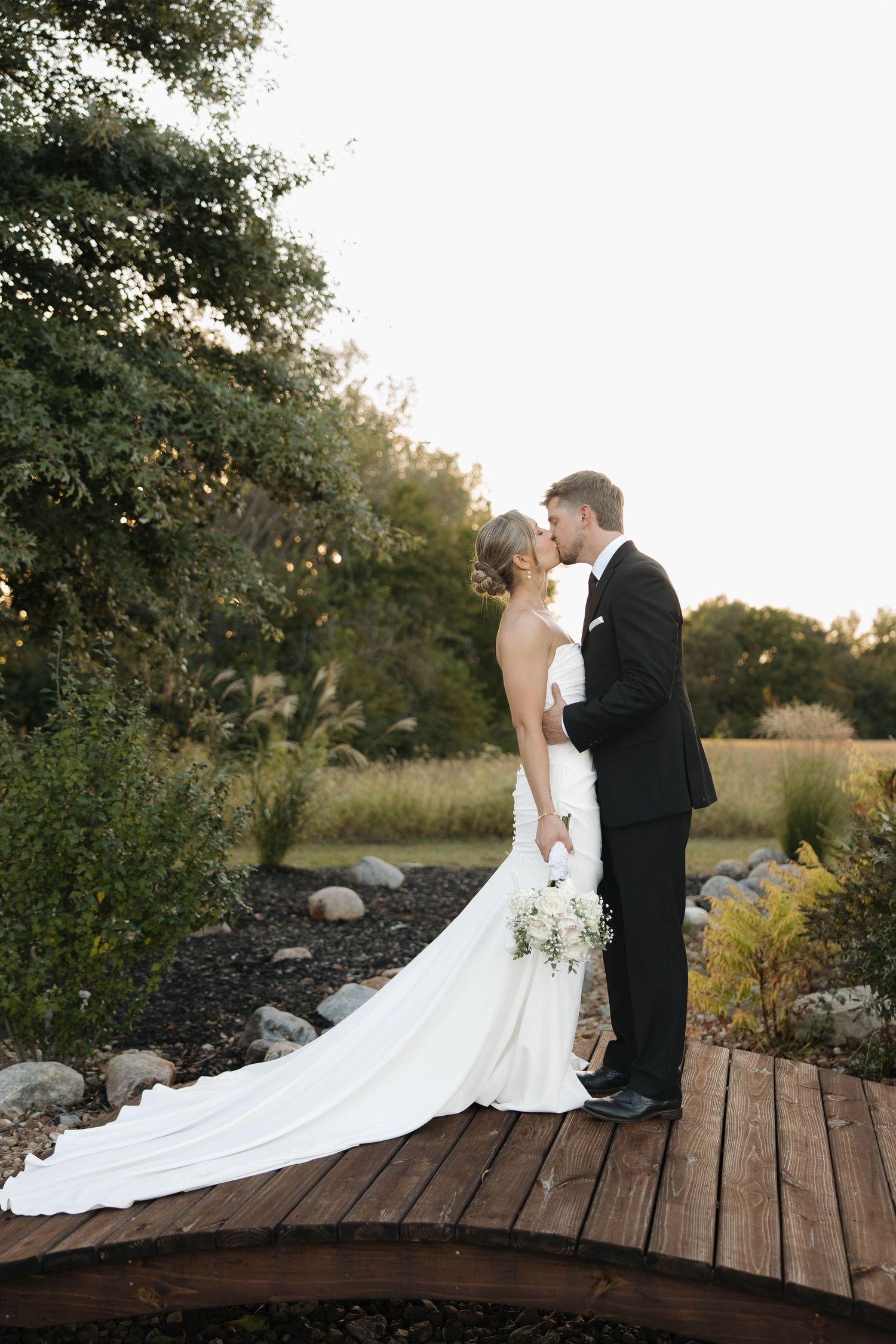 Romantic wedding portrait of couple standing on wooden bridge during golden hour.