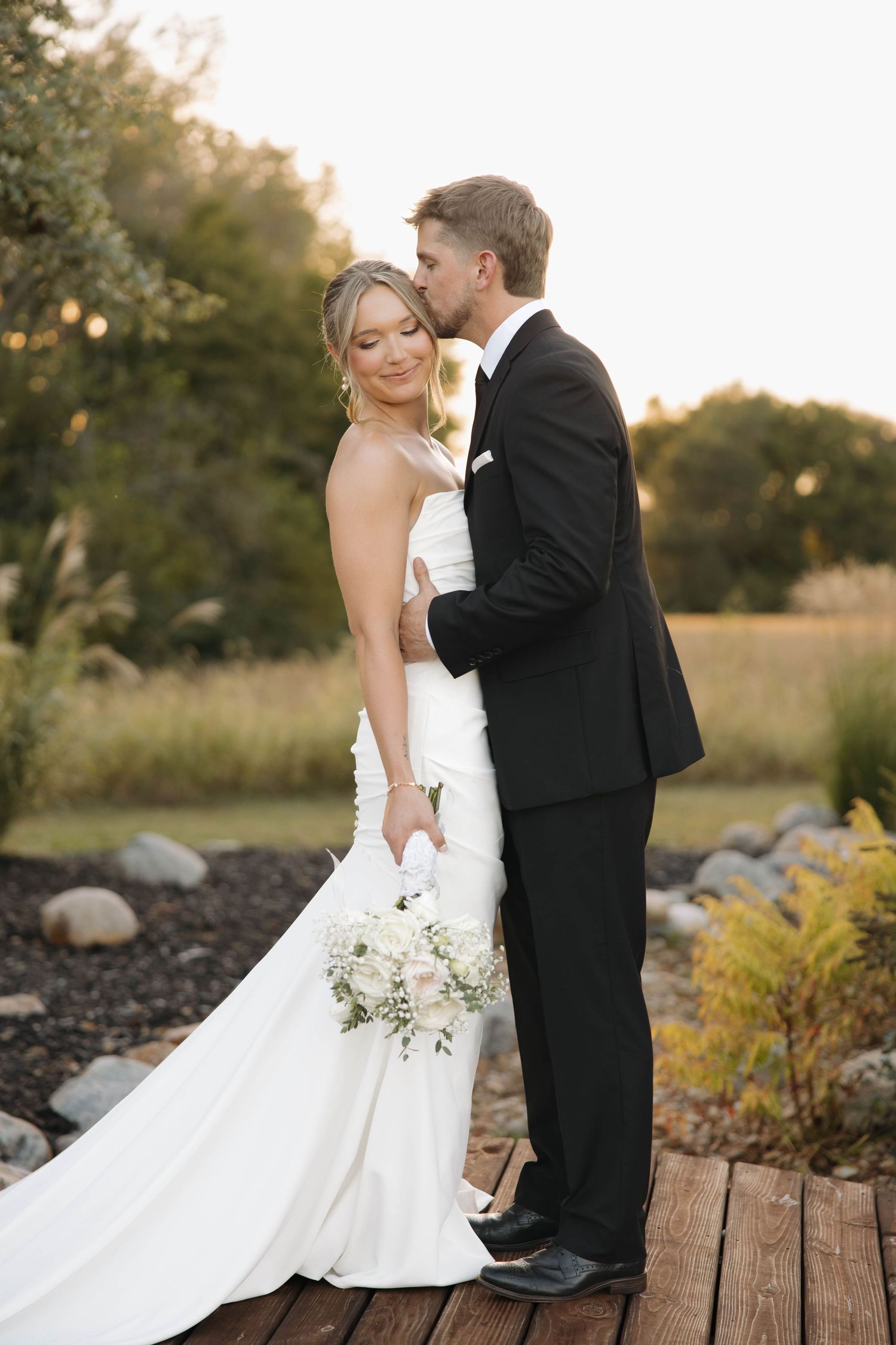 Romantic wedding portrait of couple embracing on wooden deck at sunset.