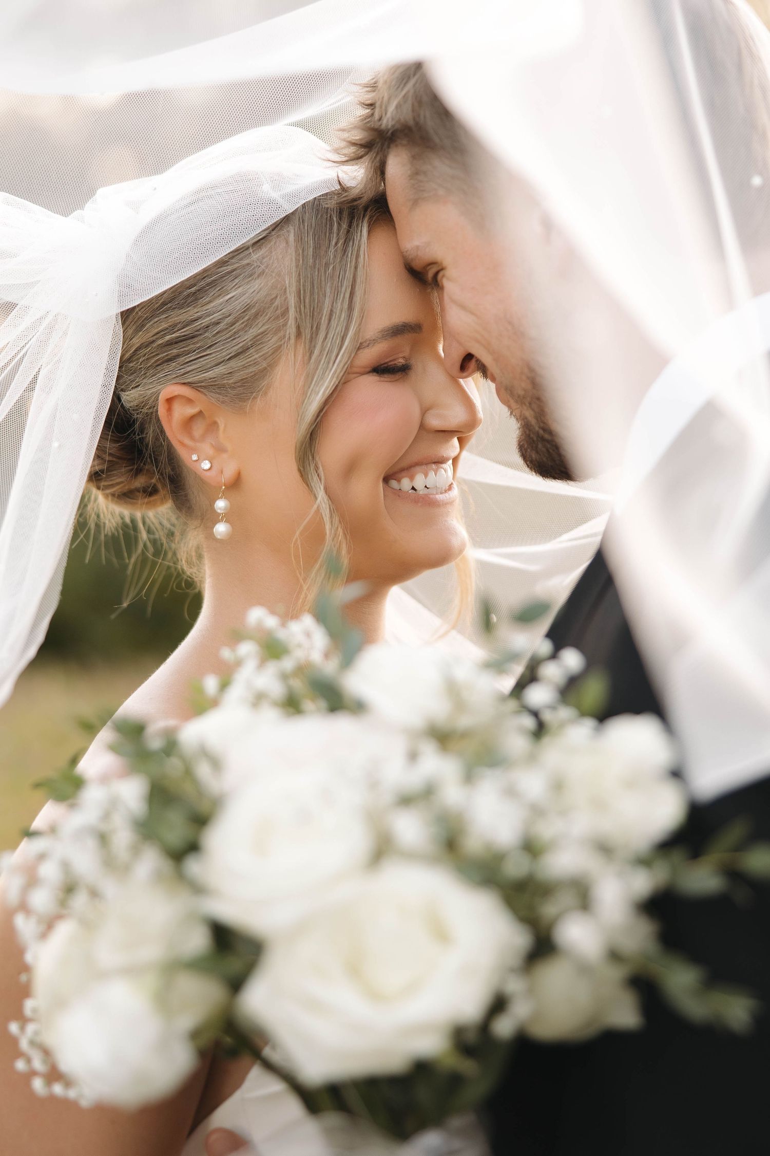 Intimate moment under a wedding veil with white roses in the foreground.