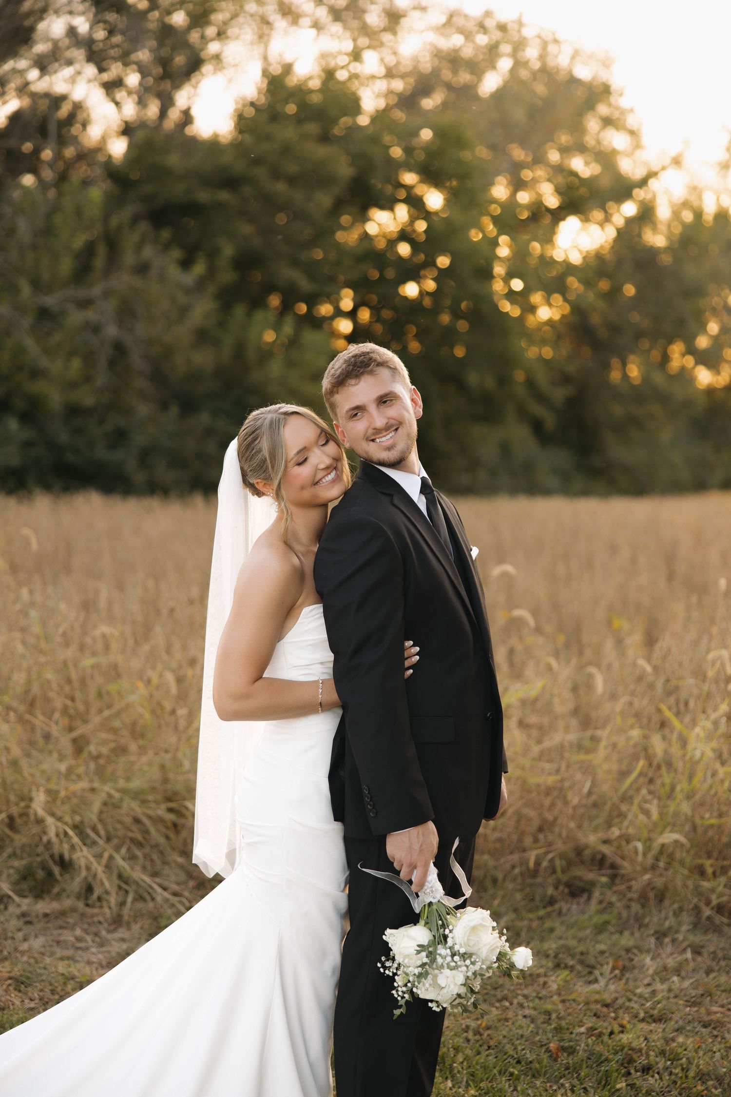 Sunset wedding portrait of a couple laughing together in a golden field.