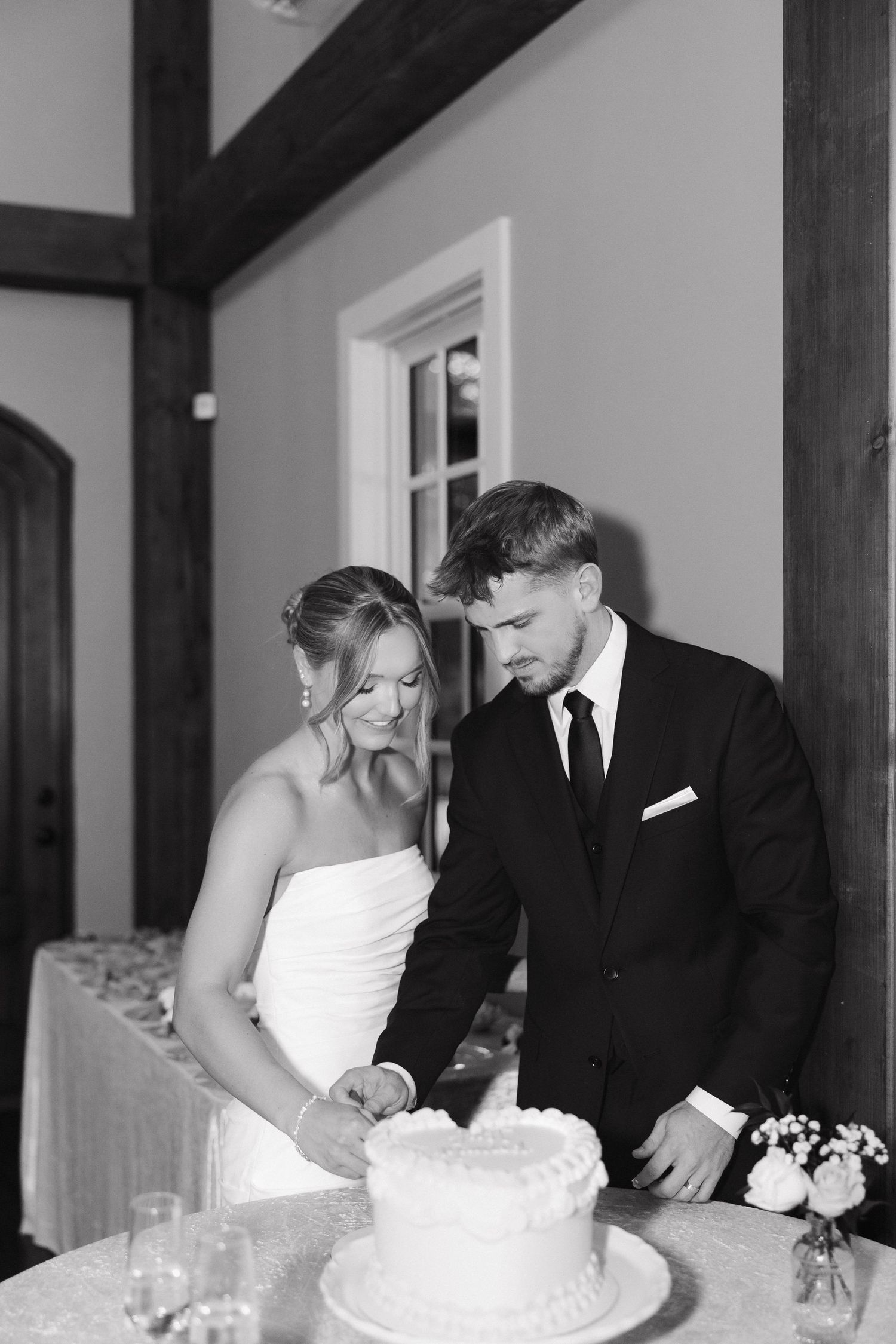 Black and white photo of a couple cutting their wedding cake at the reception.