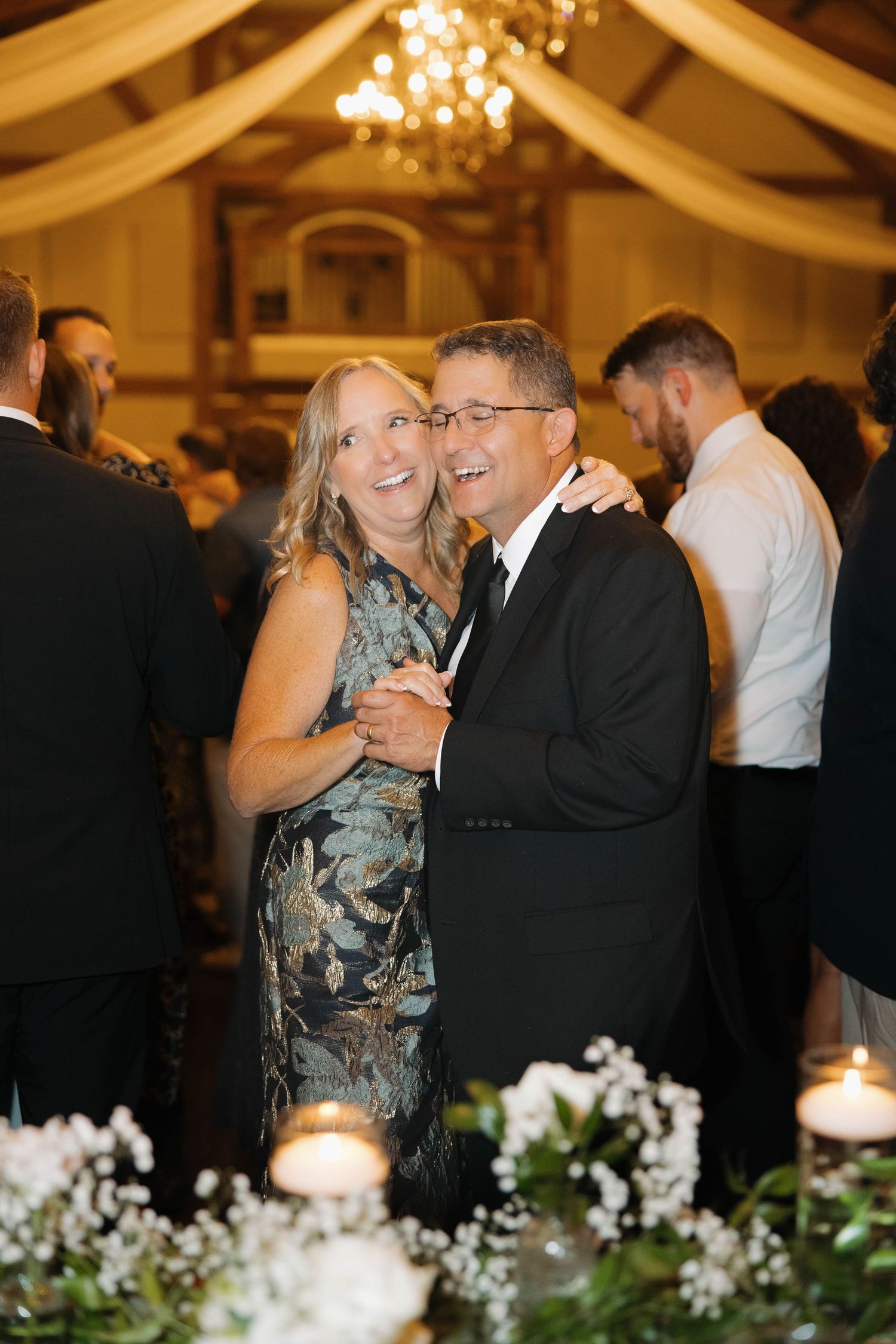 A couple shares a romantic dance together at an elegant wedding reception with draped fabric and chandeliers.
