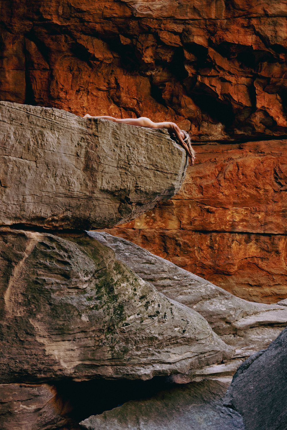 Dramatic red sandstone cliffs and rock formations create natural overhangs against a rugged desert landscape.