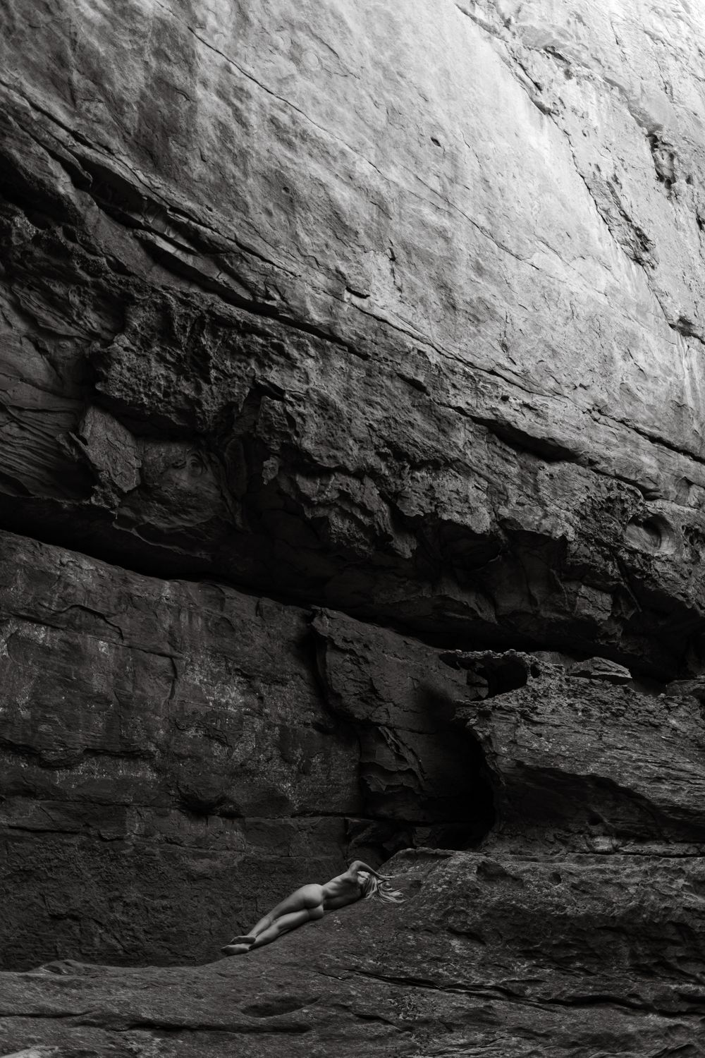 A sequence of black and white photographs showing a rock climber navigating through a challenging cave overhang.