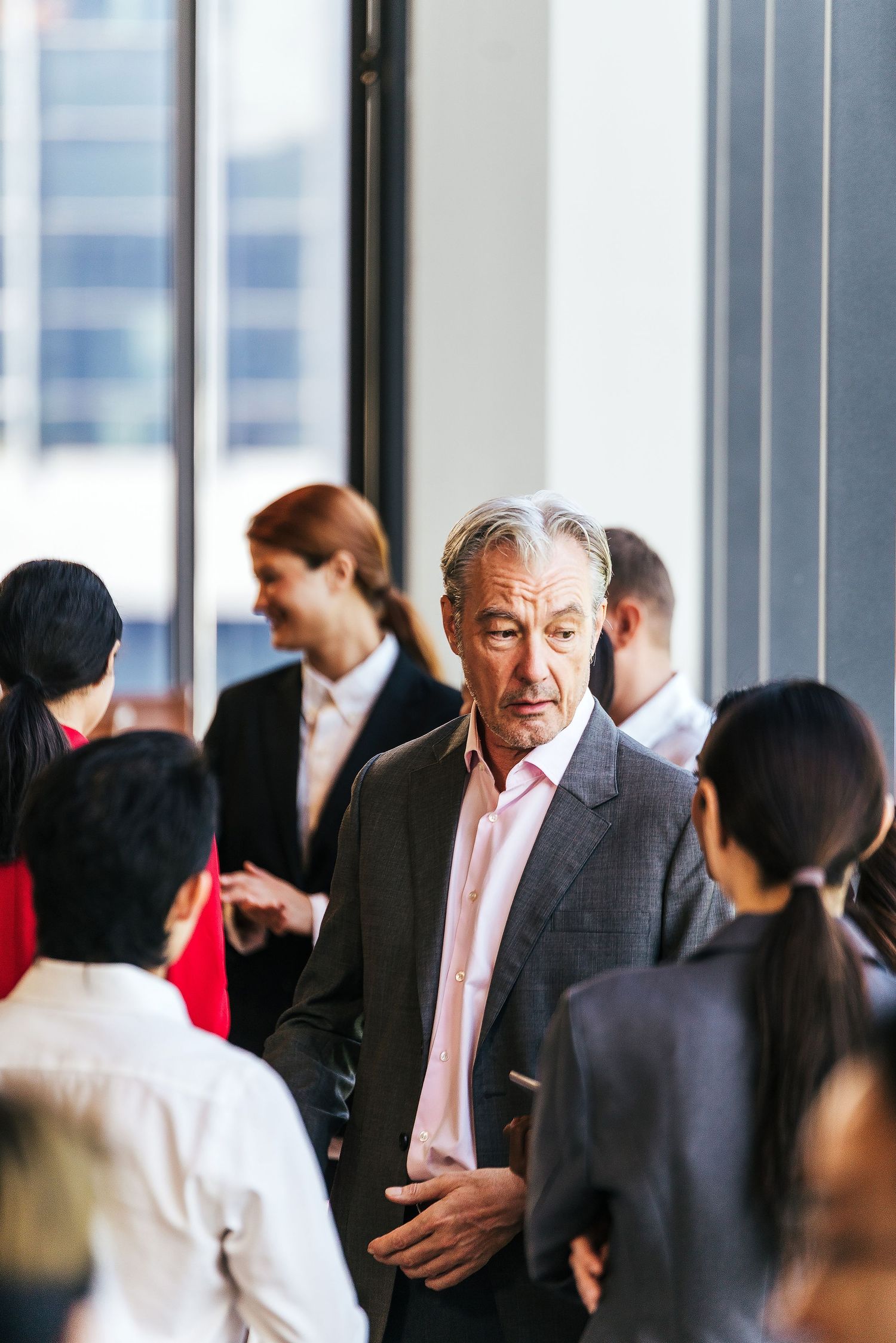 Senior businessman in a gray suit standing among colleagues networking in a modern office.