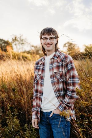 A series of outdoor portrait shots in a golden field at sunset wearing a plaid shirt and glasses.