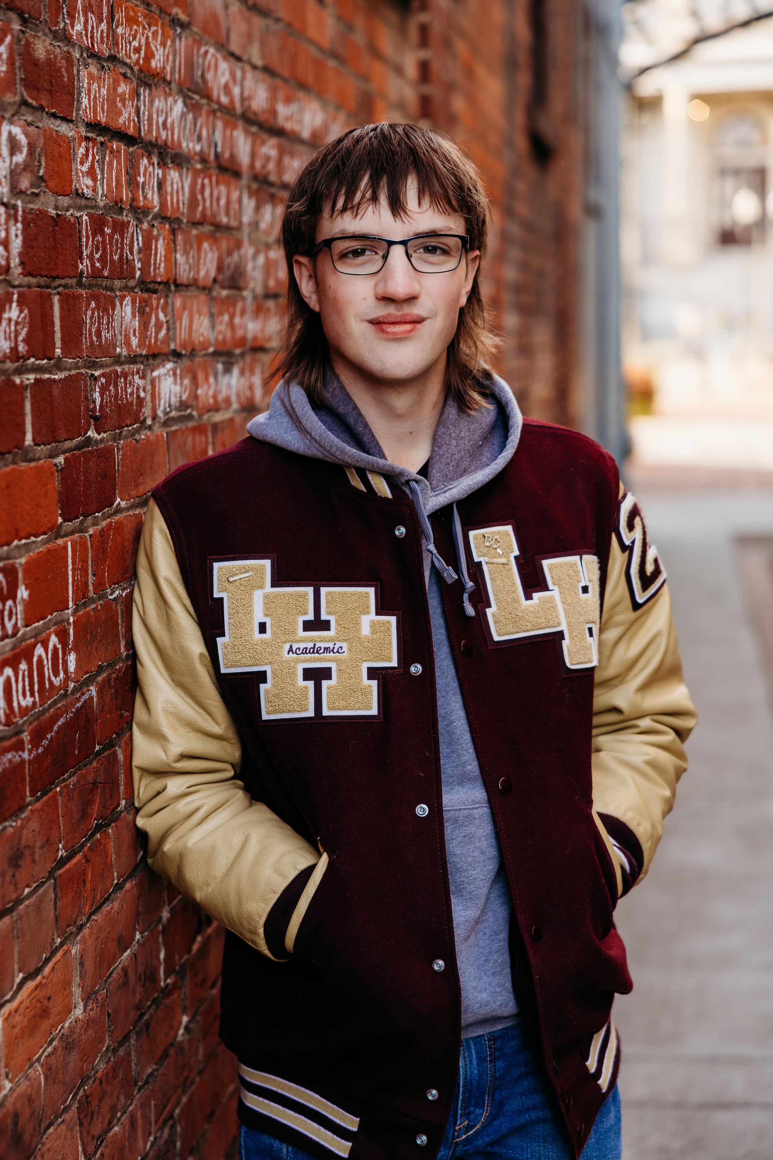 Vintage varsity letterman jacket in burgundy and tan styled against rustic brick wall background.