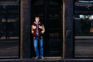 A person in jeans and a dark jacket stands in a doorway at night casting a dramatic shadow on the ground.