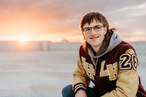 A student in a varsity letterman jacket sits outdoors during a golden sunset.