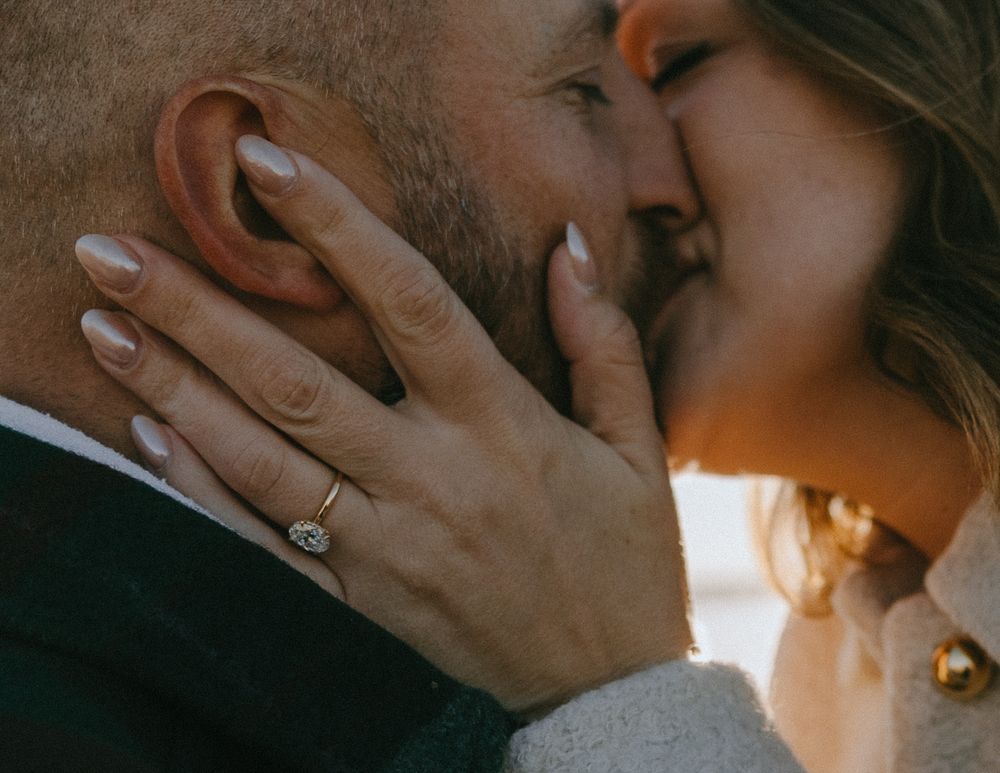 A close up intimate moment between a couple showing hands with an engagement ring in warm lighting.