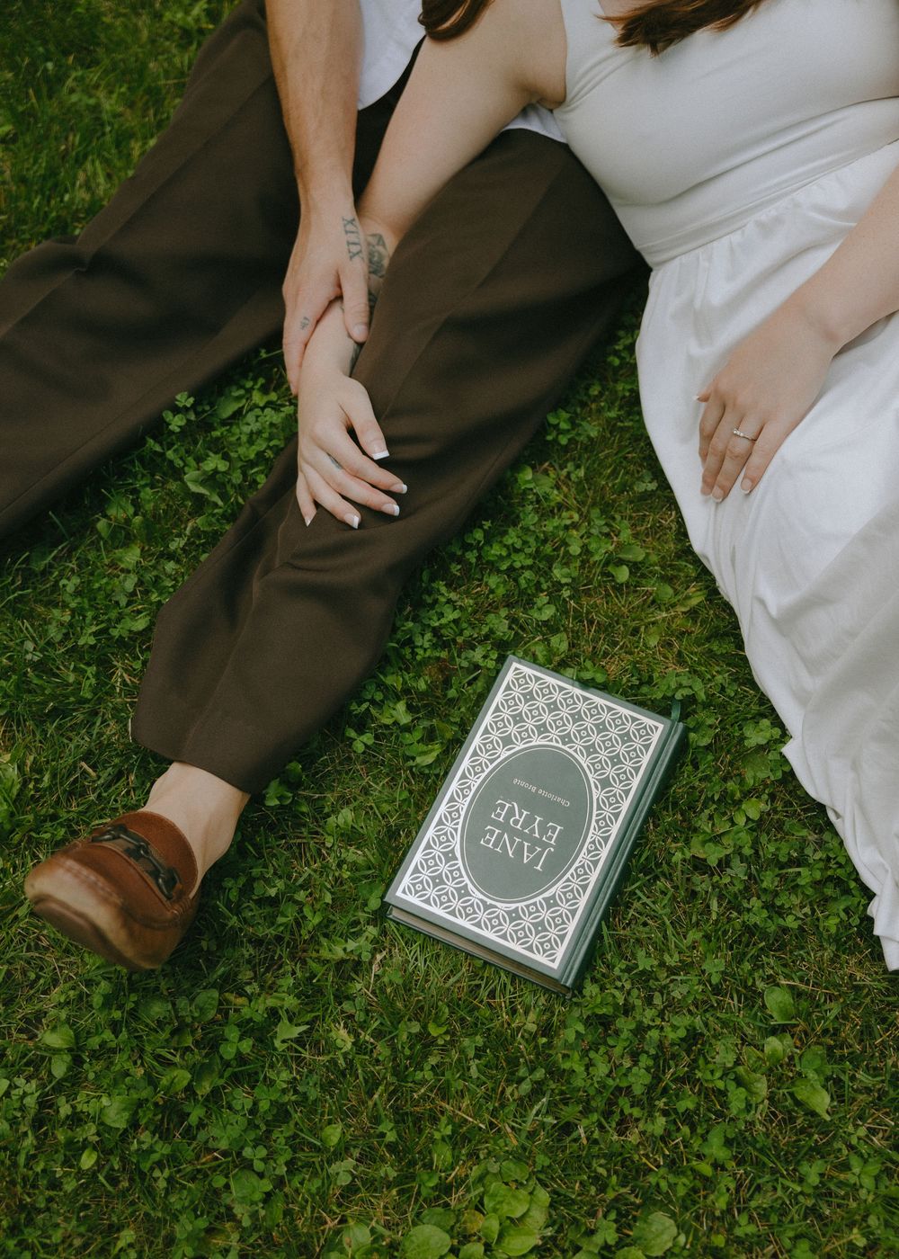 A person in brown pants and white dress lying on grass with a vintage-style book beside them.
