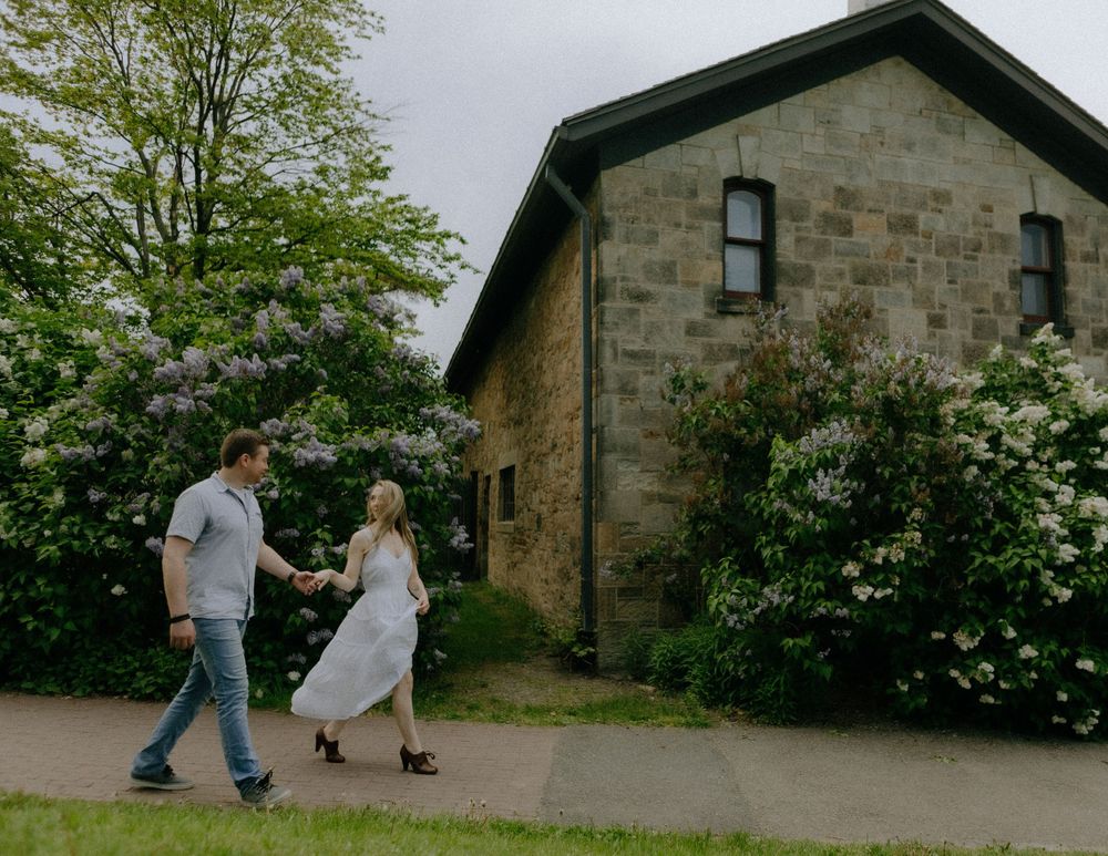 Stone house exterior with blooming spring trees and figures walking along a garden path.
