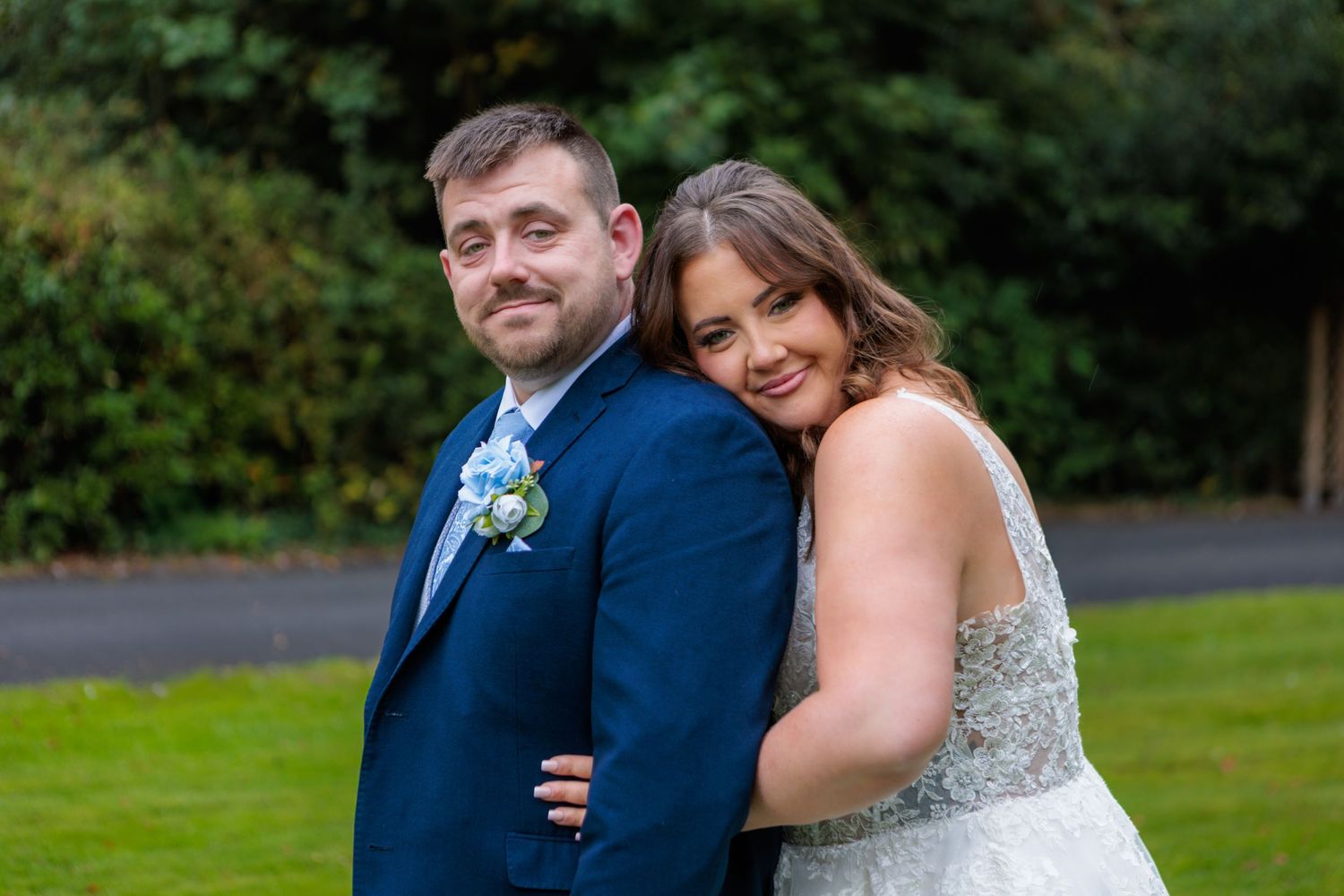 A couple poses together outdoors on their wedding day wearing a navy suit and sparkly white dress.