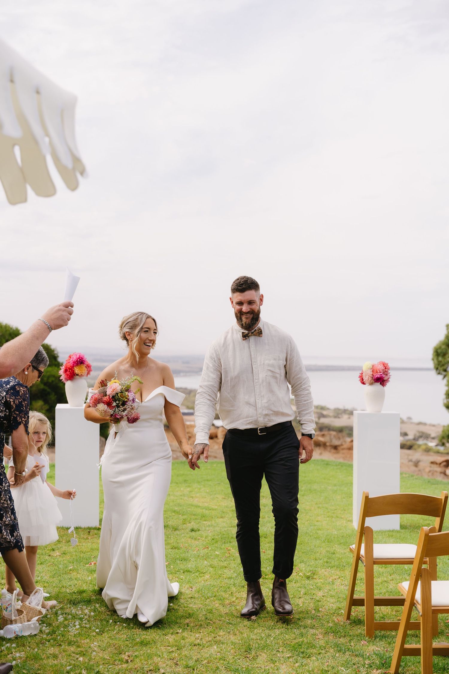 Wedding guests mingle and celebrate on a grassy lawn overlooking the ocean during an outdoor reception.