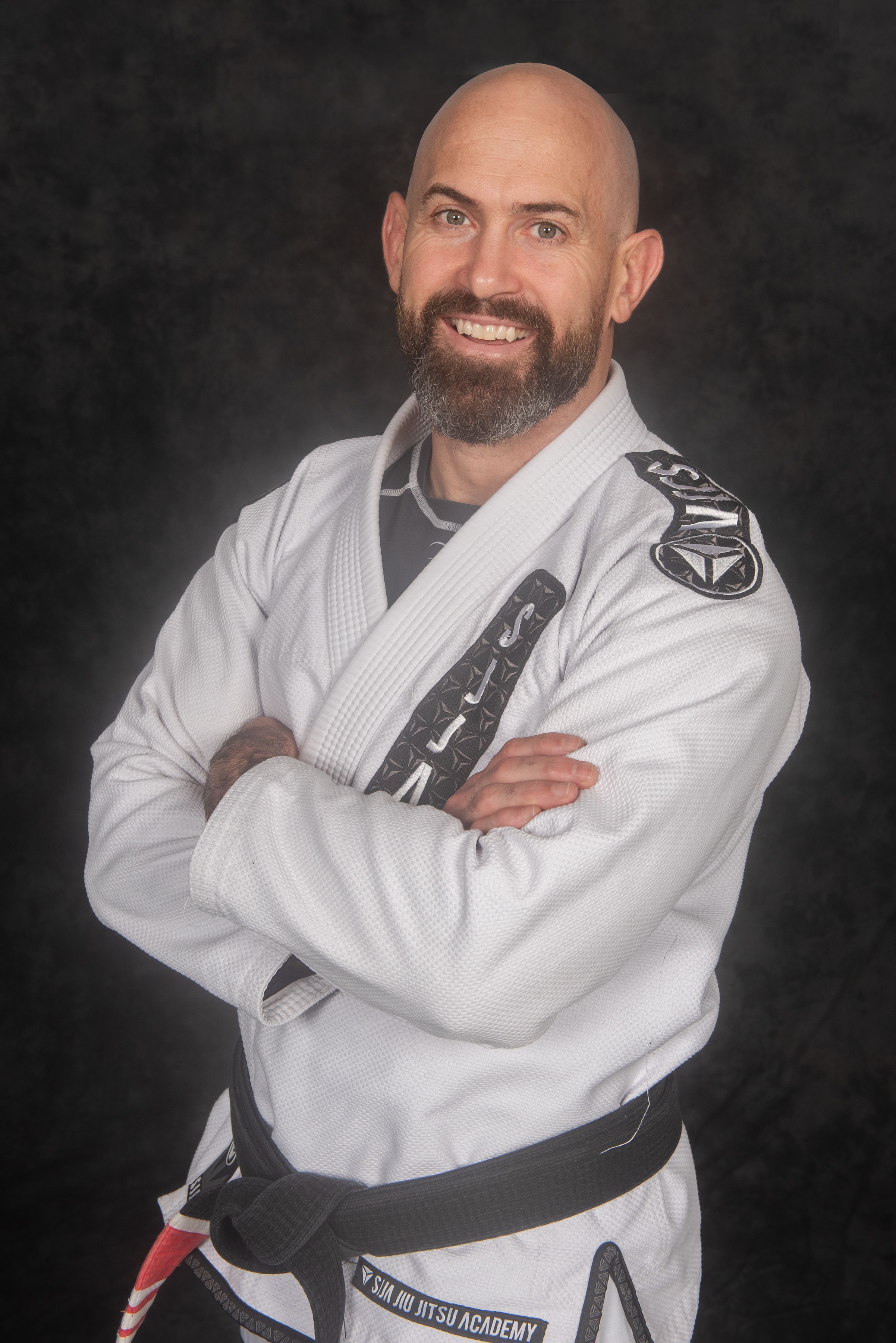 Martial arts instructor in white gi with black belt poses against dark background.