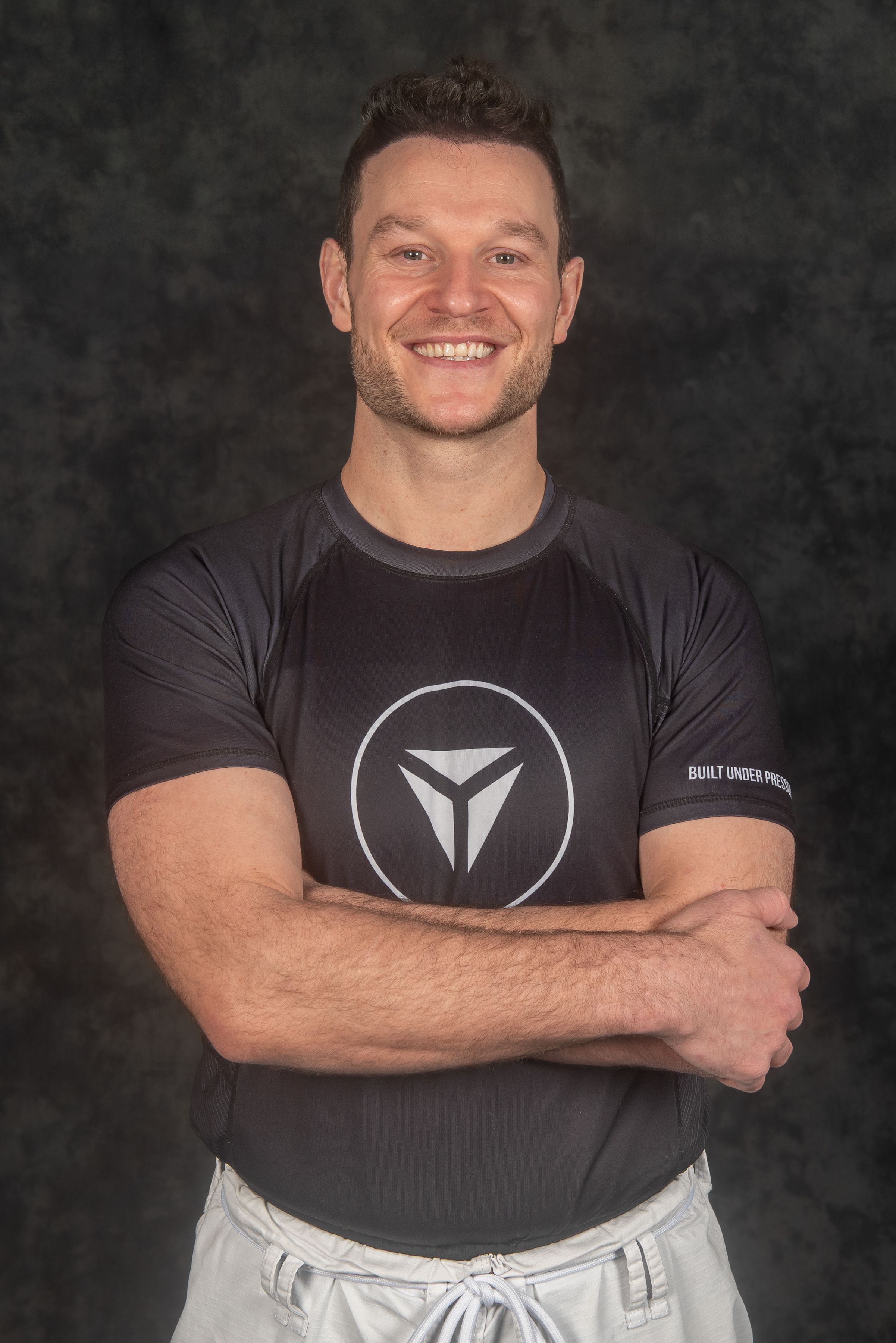 Athletic instructor in black logo shirt poses against dark background.