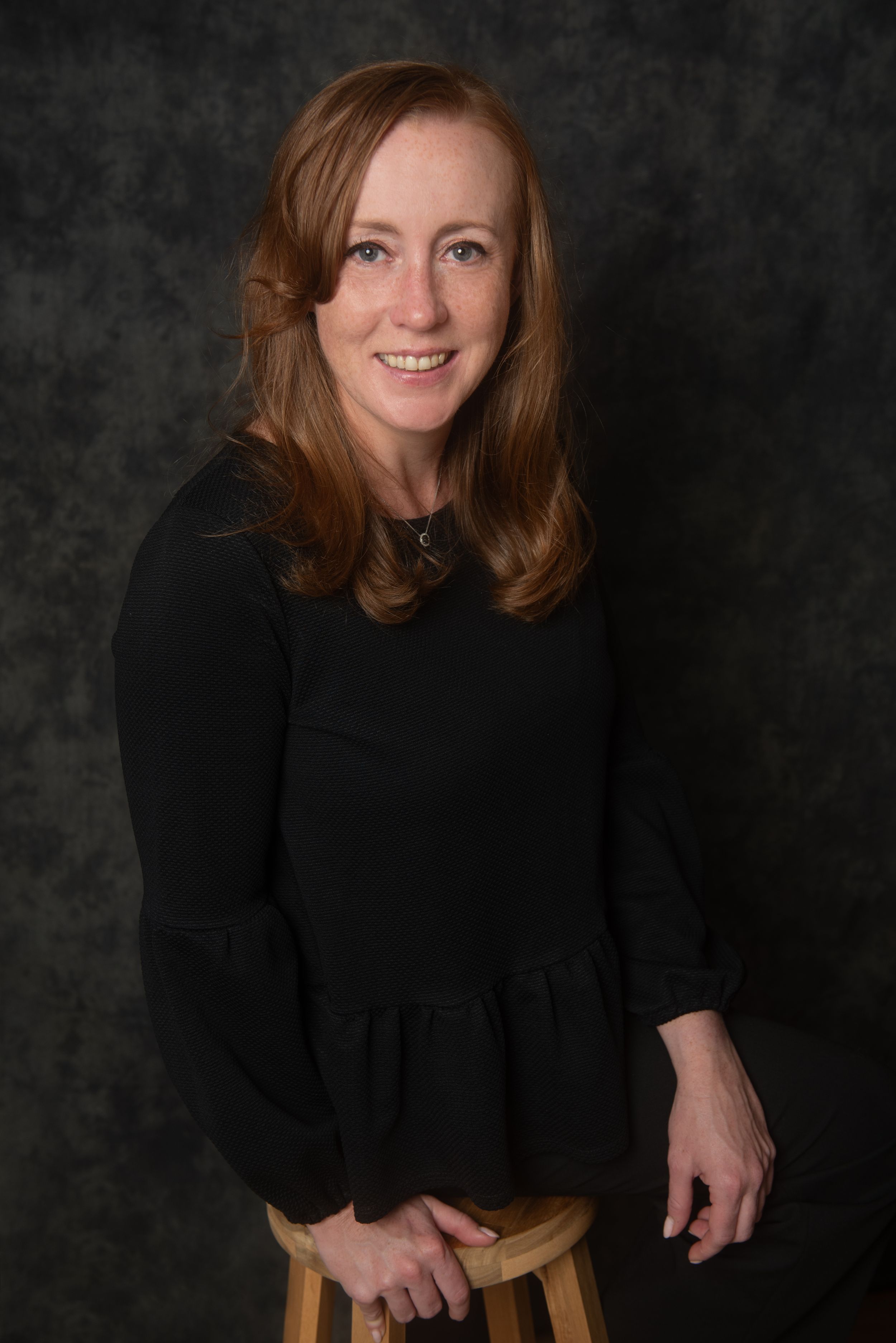 Studio portrait featuring someone in a black sweater against textured background.