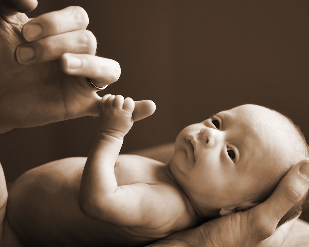 A man's hand gently holds a newborn baby in a tender moment captured by Abigail's Studio in Buckinghamshire.