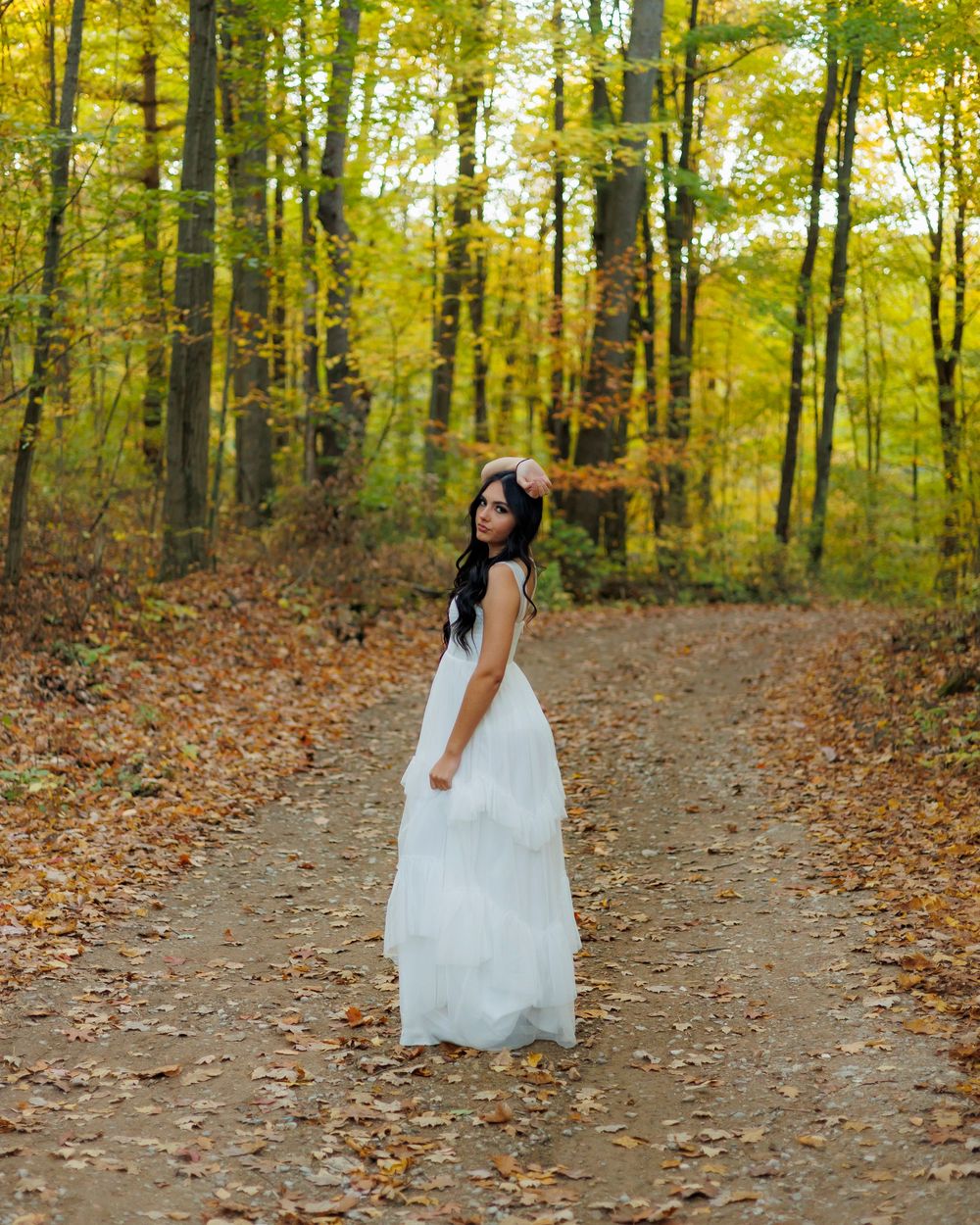 A person in a white dress walks along a forest path surrounded by golden autumn foliage.