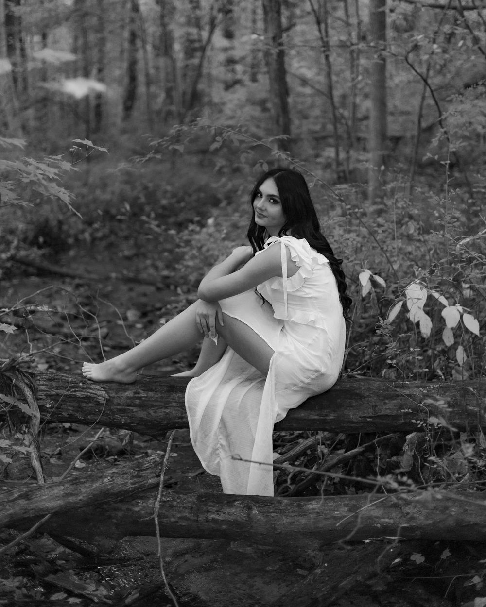 A black and white photo series shows someone in a white dress lying on fallen trees in a forest setting.