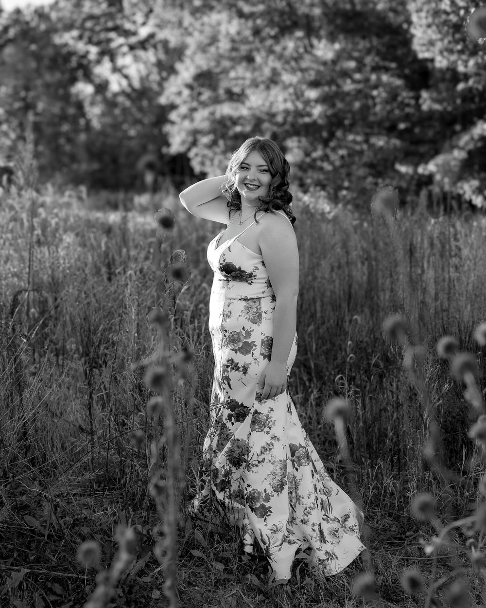 A person in a floral sundress poses gracefully in a field of tall grass and wildflowers during golden hour.
