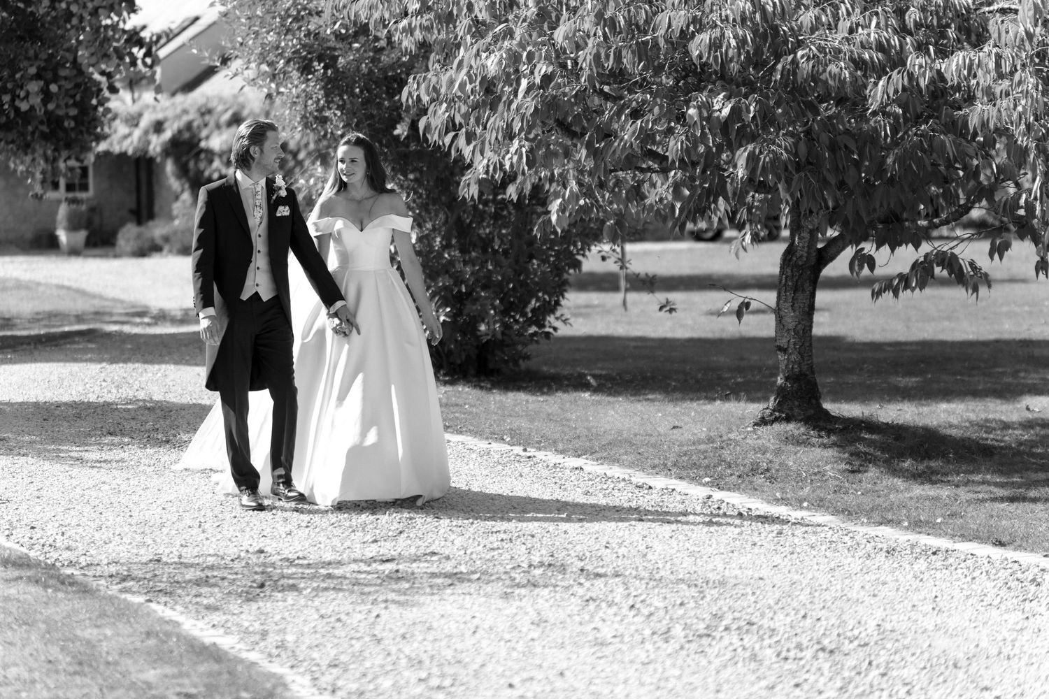 Wedding couple exits stone church archway while guests throw confetti in joyful black and white photograph.
