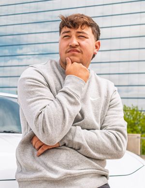 Person in gray sweatshirt poses thoughtfully against blue lined wall background.