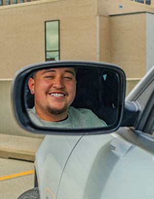 Reflection in car side mirror shows person smiling in gray shirt.