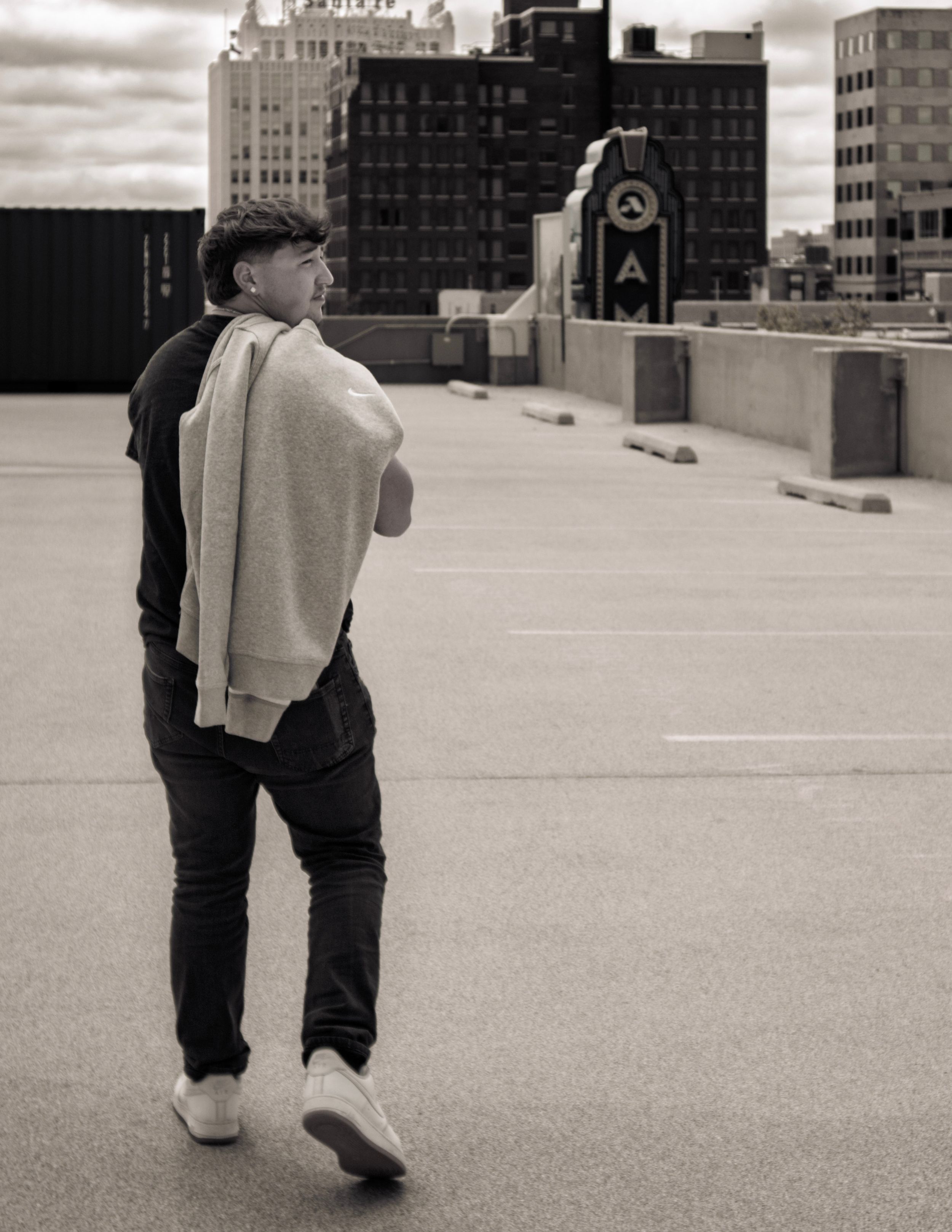 Person in casual wear walking on rooftop with city skyline in black and white.