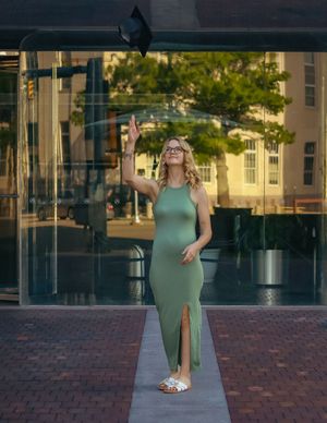 Person in a sage green dress poses on a brick walkway at sunset near modern glass buildings.