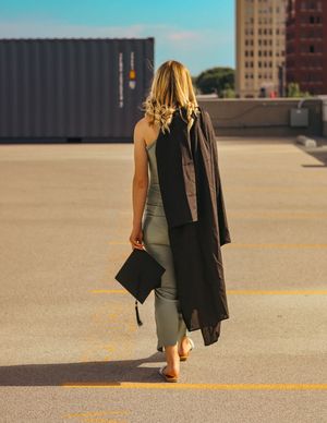 Woman carrying black bag walks across urban rooftop parking area in casual attire and long coat.