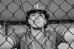 Black and white portrait through chain link fence of person in baseball uniform.