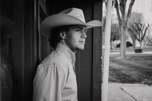 A black and white portrait of someone in western attire with a cowboy hat looking off to the side.