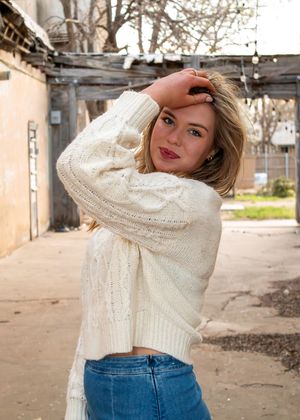 Person in a cozy cream cable knit sweater and jeans poses casually against an outdoor backdrop.