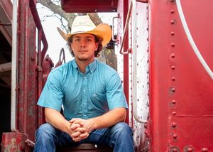 Person wearing turquoise shirt and cowboy hat sitting in red train car.